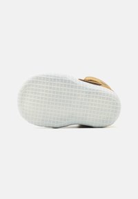 Suola in gomma bianca con motivo antiscivolo testurizzato, dotata di tomaia marrone con finitura effetto camoscio e dettagli cuciti.