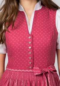 Traditionelles Kleid mit einem rosa gemusterten Oberteil, einer weißen Bluse und Spitzenakzenten. Verfügt über eine knöpfbare Vorderseite und ein gebundenes Band an der Taille.