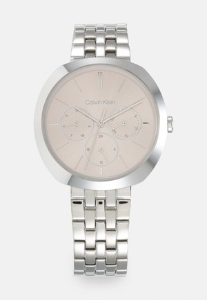 Montre en acier inoxydable argenté avec un cadran rond, un cadran beige, trois sous-cadrans et un bracelet à maillons. Présente des marqueurs d'heure minimalistes.
