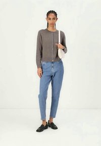 Cardigã cinza com botão sobre calças de ganga de cintura alta azul claro, combinado com mocassins pretos. Modelo segura uma pequena mochila de ombro de cor clara.