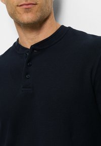 Himmelblaues Henley-Shirt aus strukturiertem Material mit einer Drei-Knopf-Leiste und kontrastierendem Halsbündchen; zeichnet sich durch ein lässiges Design aus.