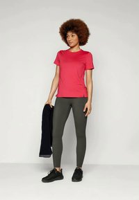 Sarkans īsām piedurknēm sporta krekls, pieguļošas pelēkas legingi, melnas kurpes. Modelis tur tumši zilā jakā, stāvot neitrālā fona priekšā.