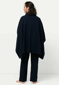 Tummansininen puuvillaponcho, jossa on korkea kaulus, rento istuvuus ja pitkät hihat, yhdistettynä vastaaviin suoriin housuihin.