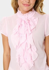 Pink ruffled blouse featuring a high collar and short sleeves, made from lightweight fabric with a soft texture and layered design.