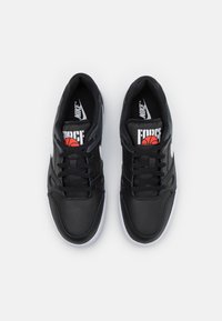 Svarta Nike-sneakers med perforerat läderöverdrag, vita accenter och en röd basketgrafik. Symmetrisk snörning med vadderad vrist.