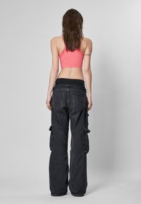 Svarte cargo-bukser med avslappet passform og sidelommer, pairing med en tettsittende rosa crop top. Glatte teksturer og kontrasterende farger er fremtredende.