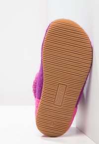 Wełniane kapcie w odcieniach purpury i różu. Gruba, teksturowana gumowa podeszwa z rowkami dla lepszej przyczepności oraz detal z logo w pobliżu pięty.