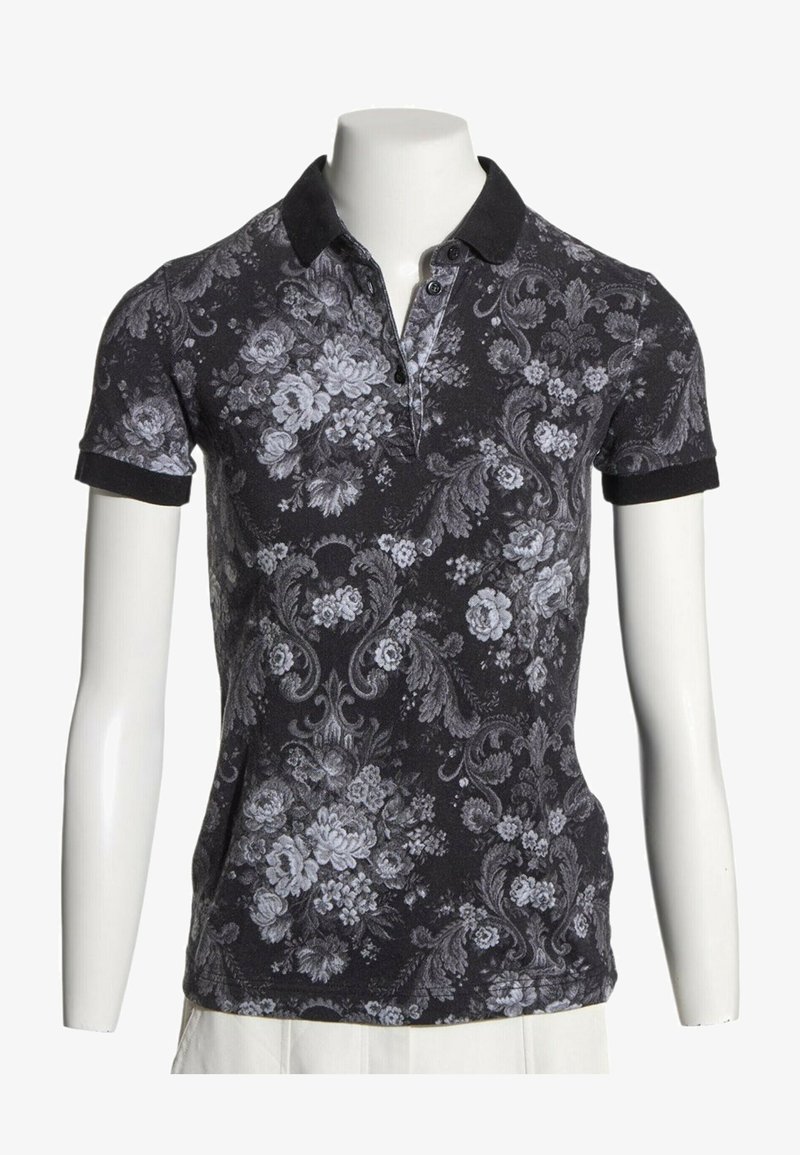 Polo noir à manches courtes avec col foncé et motif floral et ornemental gris clair sur un buste de mannequin.