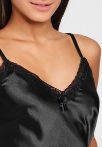 Camisole de satén negro con un ribete de encaje en el escote, que presenta detalles delicados y tirantes ajustables. La textura suave realza su elegancia.