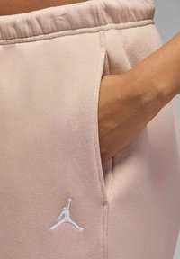 Jasnoróżowe spodnie dresowe ze ściągaczem w pasie, posiadające boczną kieszeń oraz biały haftowany logo na lewym udzie. Miękka tkanina.