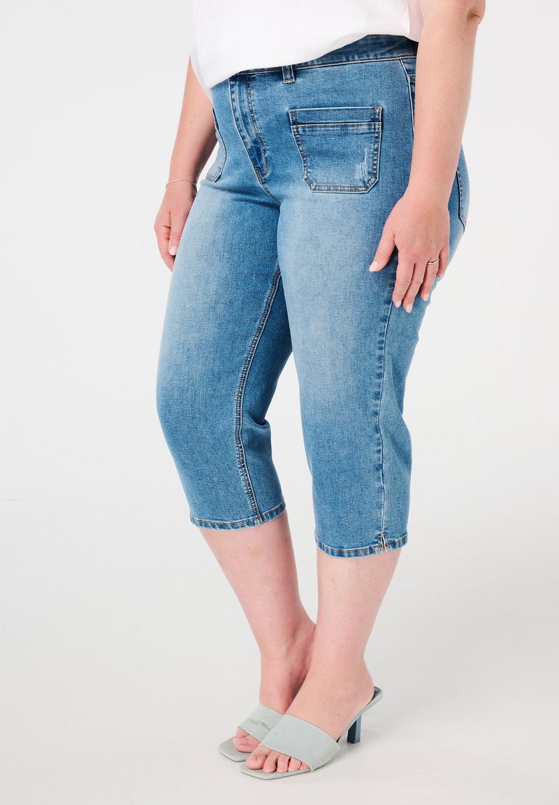 Pantalons capri en denim bleu clair avec une taille mi-haute, deux poches arrière et des poignets ourlés. Assortis à des sandales à talons bleu clair.