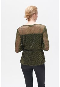 Top verde trasparente con finitura metallica, texture a righe e maniche lunghe. Adattato in vita, abbinato a pantaloni neri.