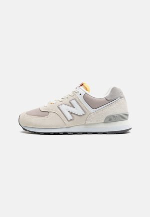 Baskets New Balance beige et grises avec logo "N" blanc, dessus en mesh et suède, semelle rembourrée et semelle extérieure texturée noire, vue de côté.