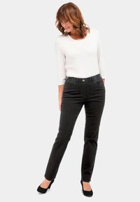 Schwarze, enganliegende Jeans mit hoher Taille, ausgestattet mit vorderen Taschen, einem Knopfverschluss und einem leichten Stretch für zusätzlichen Komfort. Dazu wird ein weißes Langarmhemd getragen.