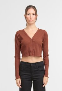 Smešani smeđi dugi rukavi uski top s V-izrezom i zatvaranjem na šest gumba. Detalj sirovog rub. U kombinaciji s crnim hlačama.