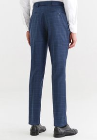 Niebieskie spodnie w kratę o gładkiej fakturze, z bocznymi kieszeniami i zapięciem na guzik z tyłu, noszone z czarnymi eleganckimi butami.
