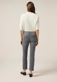 Jeans de mezclilla gris con un corte ajustado, dos bolsillos traseros y una etiqueta de cuero en la cintura. Combinados con una blusa blanca de manga corta.