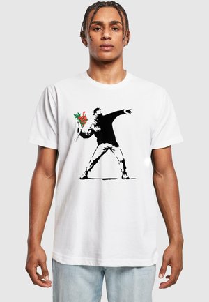 Hvid bomulds T-shirt med en sort silhuet af en figur, der kaster en buket af røde og grønne blomster. Afslappet pasform.