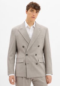 Hellgrau double-breasted Blazer aus strukturiertem Stoff, mit zwei vorderen Taschen und dunklen Knöpfen. Darunter ein weißes Hemd mit Kragen.