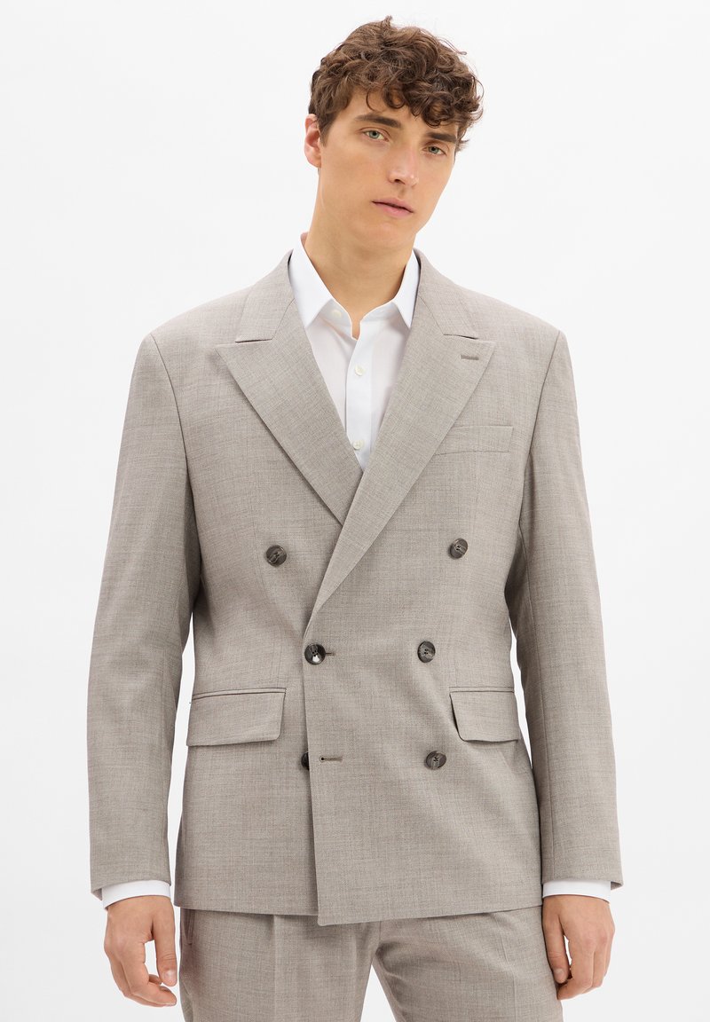 Hellgrau double-breasted Blazer aus strukturiertem Stoff, mit zwei vorderen Taschen und dunklen Knöpfen. Darunter ein weißes Hemd mit Kragen.