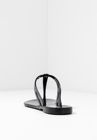 Infradito neri con suola piatta, dotati di due cinturini lucidi che formano una forma a Y. Texture liscia, design minimalista e materiale resistente.