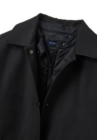 Schwarze Jacke aus glattem Stoff mit einem Kragen. Verfügt über einen Reißverschluss, Druckknöpfe und eine gesteppte Innenfütterung. Etikett innen sichtbar.