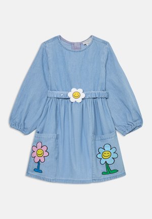 Vestido de ganga em azul claro, com mangas longas, apresentando remendos florais em rosa e azul com rostos sorridentes, e uma fivela de cinto em forma de flor.