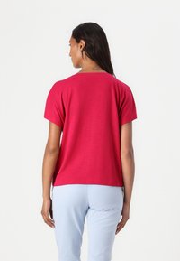 Kurzärmliges, magentafarbenes Oberteil aus einem weichen Stoff. Es hat eine lässige Passform und einen runden Halsausschnitt, kombiniert mit hellblauen Hosen.