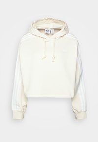 Kraftig krämfärgad hoodie i mjukt tyg, med vita randiga detaljer på ärmarna och en framficka i kängurustil. Justerbar dragsko i huvan.