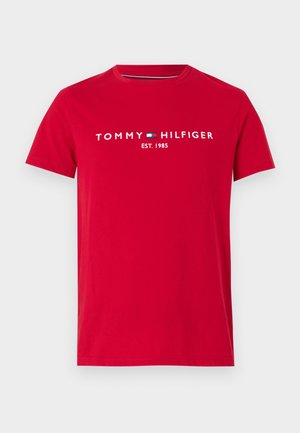 Czerwona bawełniana koszulka z krótkim rękawem i okrągłym dekoltem. Posiada białe napisy "TOMMY HILFIGER" oraz logo, a poniżej logo znajduje się napis "EST. 1985".