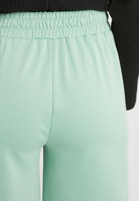 Ljus mintgröna sweatpants med resårmidja, slät textur och avslappnad passform. Synlig sömmar längs sömmen.