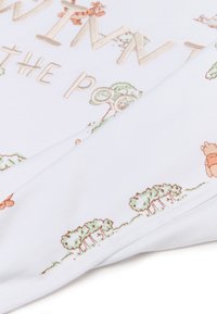 White fabric featuring embroidered text "Winnie the Pooh." Decorated with colorful cartoon trees and characters along the hem. Soft texture.