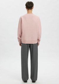 Roze gebreide trui met een ronde hals, lange mouwen en een geribde zoom, gecombineerd met grijze broek met wijde pijpen en zwarte schoenen.