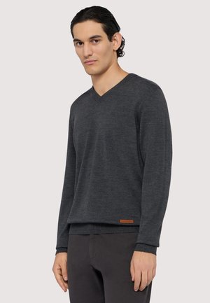 Pull en V gris foncé en tissu doux. Poignets et ourlet côtelés, avec un petit logo en cuir marron en bas à gauche.