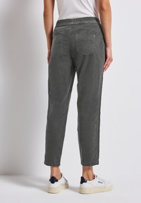Grijze rechte broek met een textuurstof, elastische tailleband en twee achterzakken, gecombineerd met witte sneakers.
