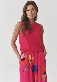 Top de tirantes rosa brillante con un diseño de punto texturizado, acompañado de una falda a juego con un patrón floral colorido y bolsillos.