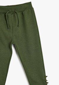 Grüne Jogginghose aus weichem Stoff mit einem Kordelzugbund und spikeartigen Akzenten entlang des äußeren Oberschenkels.