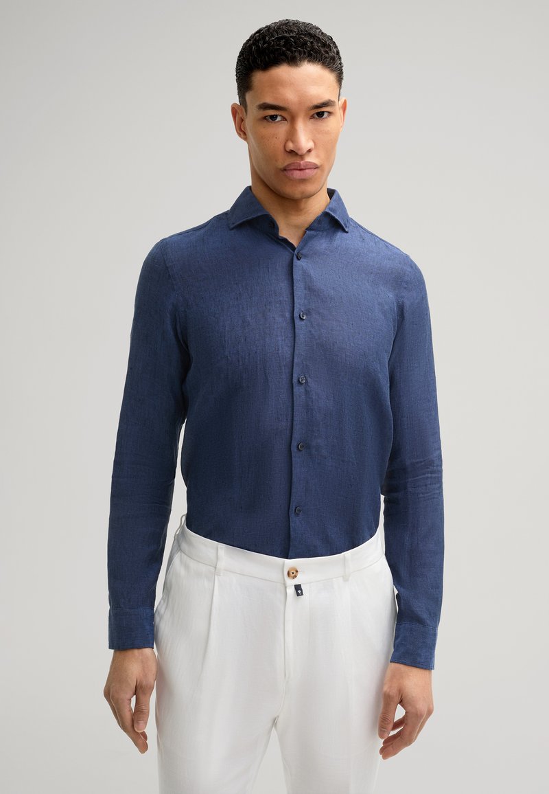 Dunkelblaues Langarmhemd aus strukturiertem Stoff, mit einem Button-down-Kragen und passenden Knöpfen, kombiniert mit weißen Leinenhosen.