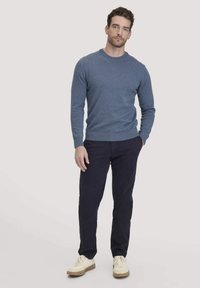 Blauer Pullover mit Rundhalsausschnitt, aus einem weichen Stoff, kombiniert mit navyfarbigen Hosen und weißen Schuhen, vor einem hellen Hintergrund stehend.