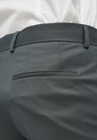 Γκρίζα, προσαρμοσμένα παντελόνια με λεία υφή. Διαθέτουν μία πίσω τσέπη και λεπτή ζώνη. Σχεδιασμένα με διακριτές κάθετες ρίγες.