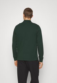 Long-sleeve polo shirt in dark green cotton with a collar, slim fit, and ribbed cuffs, featuring a clean, solid design.