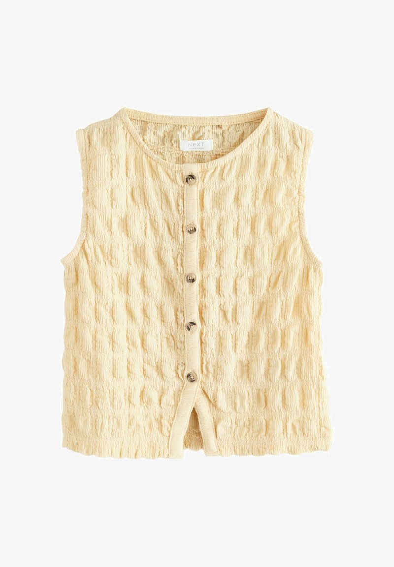 Haut beige sans manches avec texture, boutonné sur le devant, col rond et cinq boutons au centre.