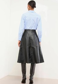 Must muströödest midi seelik, millel on laienev disain ja selja tõmblukk, koos siniste triipudega nööpidega pluriga. Sile tekstuur, struktureeritud siluett.