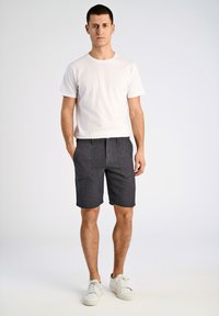 Witte crewneck t-shirt gecombineerd met grijze shorts met textuur, verticale strepen en zakken, afgemaakt met witte sneakers.