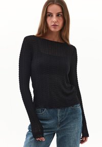 Sort langærmet sweater med et tekstureret mønster, der har en bred halsudskæring og en tætsiddende silhuet, parret med falmede blå jeans.