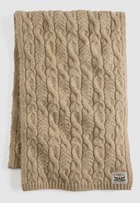 Béžový vlnený šál s vrkočovým vzorom, štruktúrovaným povrchom a rebrovaným okrajom. Na spodnej časti je malá značková nášivka.
