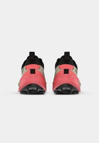 Παπούτσια trail running με μαύρο επάνω μέρος, με μπεζ λεπτομέρειες και φωτεινή ροζ φτέρνα. Κείμενη μαύρη σόλα για πρόσφυση, με ανθεκτικό σχέδιο.
