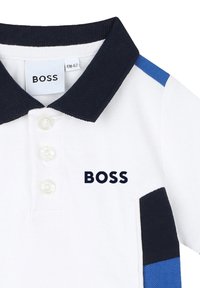 Polo bianco con colletto blu navy, tre bottoni e logo "BOSS". Dettagli in tessuto blu navy e blu sulle maniche per un contrasto.