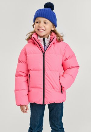 Giacca a vento rosa con zip frontale, dettagli neri e cappuccio. Indossata sopra un maglione grigio chiaro, abbinata a jeans blu e a un berretto di lana blu.