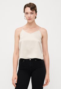 Krem satin cami med tynne stropper, V-hals og løs passform, kombinert med svarte jeans. glatt tekstur, enkelt design, ingen mønstre.